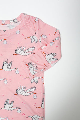 A pink long-sleeve baby t-shirt with an all-over print of white storks carrying white bags, photographed against a plain white background.