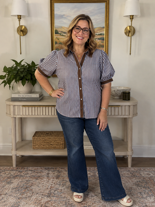 A woman modeling a short-sleeve button-up shirt with vertical blue and white stripes, brown trim
