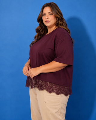 A woman modeling a short-sleeve maroon top with a lace hem, paired with beige pants