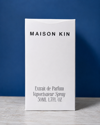 Maison Kin perfume bottle with silver cap on a blue background