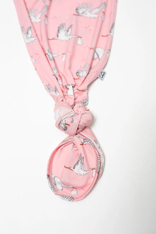 A pink fabric headwrap or scarf with a printed pattern of white storks and gray leaves, tied in a knot at the bottom, shown against a plain white background.