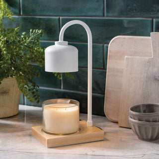 White lamp with a candle on a wooden base in front of green tiled wall and wooden cutting boards.