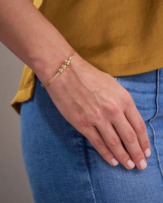 Person wearing a gold bracelet on a neutral background