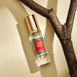 Perfume bottle with gold cap and red label on a beige surface with a branch in the background