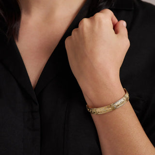 Gold bracelet on a person's wrist against a black background
