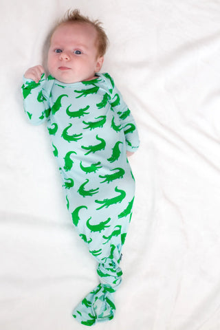 Baby wearing a light blue onesie with green alligator pattern on a white background