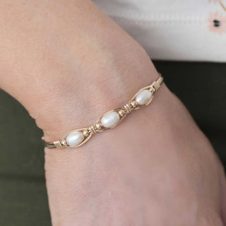 Gold bracelet with pearl-like beads on a wrist against a neutral background