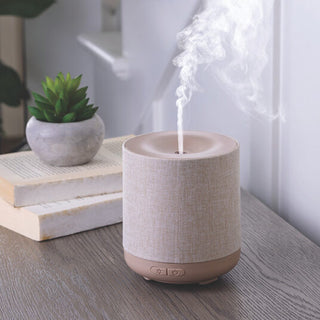 Textured diffuser emitting mist on a wooden surface with a plant and books in the background