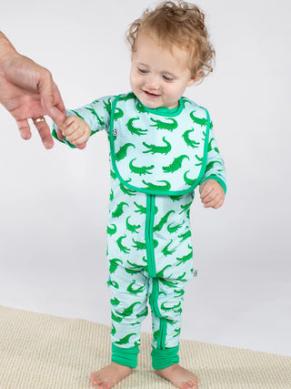Baby wearing a green and white alligator-patterned onesie on a plain background