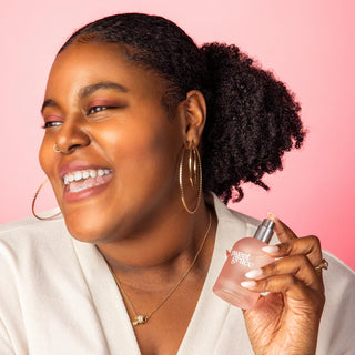 Woman holding a perfume bottle against a pink background