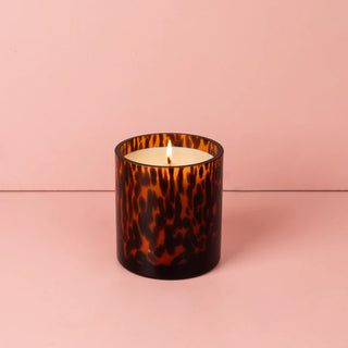 Candle in a tortoiseshell-patterned glass container on a pink background