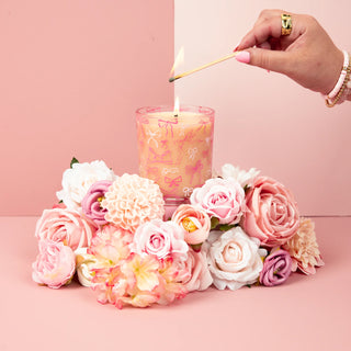 Candle being lit with a match, surrounded by pink and white flowers on a pink background