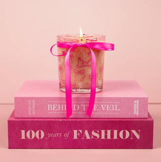Candle with a pink ribbon on top of two books against a pink background
