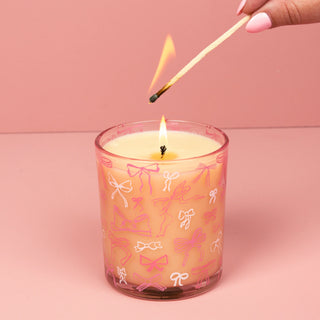 Candle with bow pattern being lit with a match on a pink background