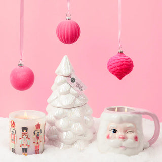 Decorative Christmas scene with a white ceramic tree, Santa face mug, and pink ornaments on a pink background.