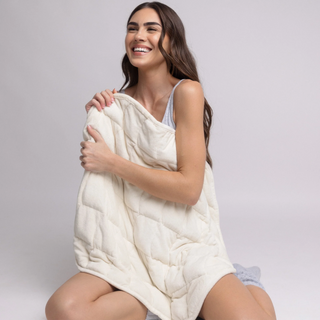 Woman holding a white quilted blanket against a plain background