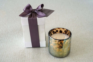 Candle with leopard print design next to a gift box with a purple ribbon on a light gray background