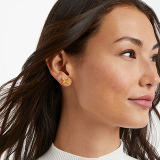 Close-up of a woman wearing gold butterfly earrings with a neutral background