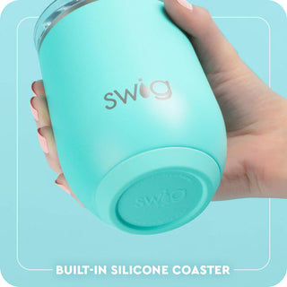 Hand holding a turquoise Swig tumbler with a built-in silicone coaster on a light blue background.