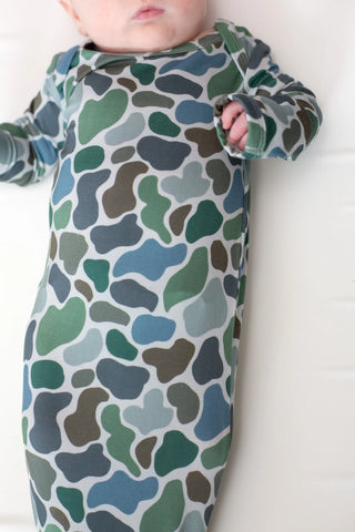 A baby wearing a long-sleeve sleep sack with a green, blue, and brown organic camouflage pattern on a white background.