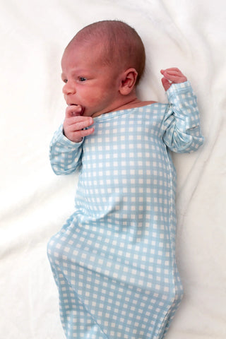 Newborn baby wearing a blue checkered outfit on a white blanket