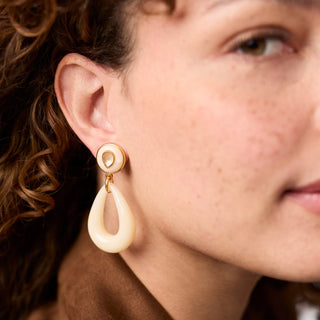 Close-up of a person wearing a gold and cream earring.