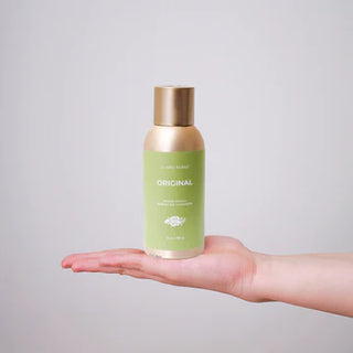 Hand holding a green bottle labeled 'Original' against a gray background