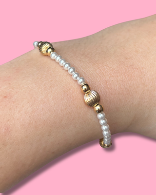 Bracelet with gold and pearl beads on a wrist against a pink background