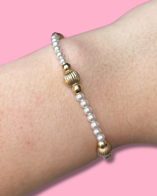 Pearl and gold beaded bracelet on a wrist with a pink background