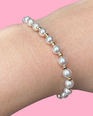 Pearl bracelet with gold accents on a wrist against a pink background