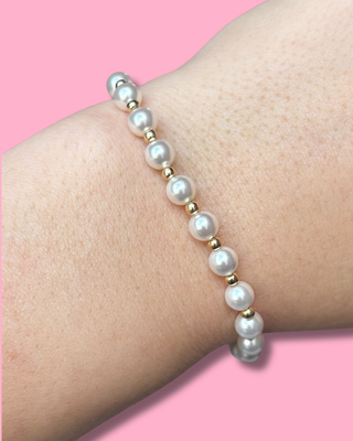 Pearl bracelet on a wrist with a pink background
