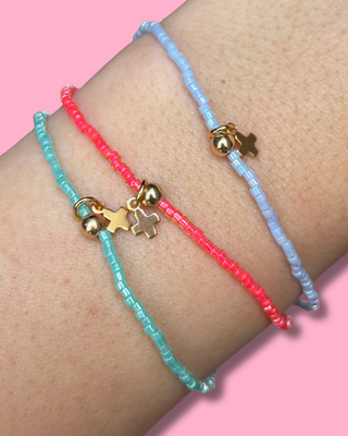 Two beaded bracelets with gold charms on a wrist against a pink background