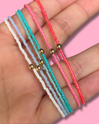 Three colorful beaded bracelets on a hand with a pink background