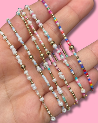 Colorful beaded bracelets on a hand with a pink background