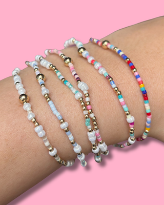 Multicolored beaded bracelets on a wrist against a pink background