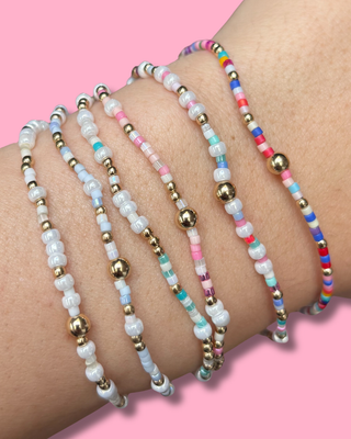 Multicolored beaded bracelets on a wrist with a pink background