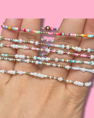 Colorful beaded bracelets on a hand with a pink background
