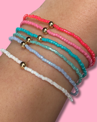 Multicolored beaded bracelets on a wrist with a pink background