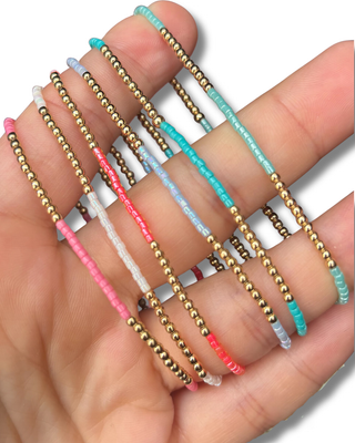 Hand holding multiple beaded bracelets of different colors on a white background