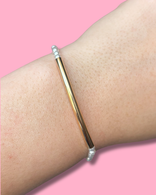 Gold and silver beaded bracelet on a wrist against a pink background