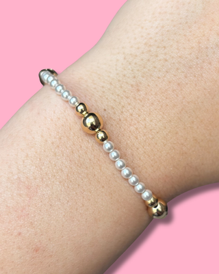 Bracelet with gold and pearl beads on a wrist against a pink background