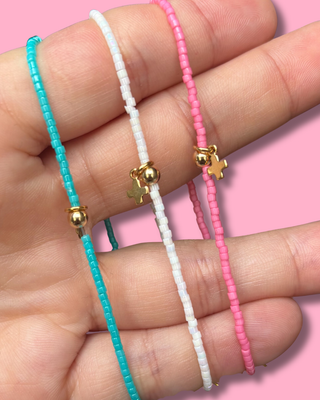 Three colorful beaded bracelets with gold beads on a hand against a pink background