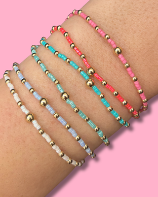 Three beaded bracelets on a wrist against a pink background