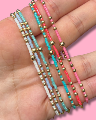 Three colorful beaded bracelets on a hand with a pink background