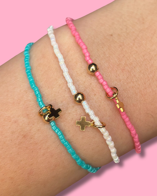 Three colorful beaded bracelets on a wrist against a pink background