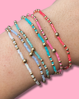 Set of colorful beaded bracelets on a wrist with a pink background
