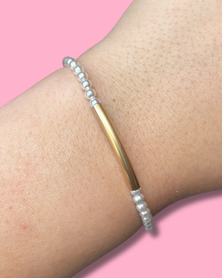 Bracelet with gold bar and pearl-like beads on a wrist against a pink background