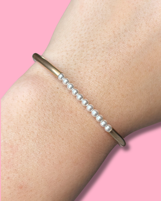 Pearl bracelet on a wrist with a pink background