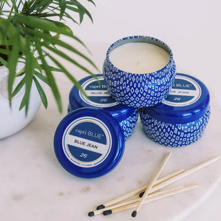 Capri Blue candles with blue and white patterned lids on a marble surface with a plant in the background.