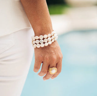 Hand wearing multiple pearl bracelets with a gold ring on a blurred background